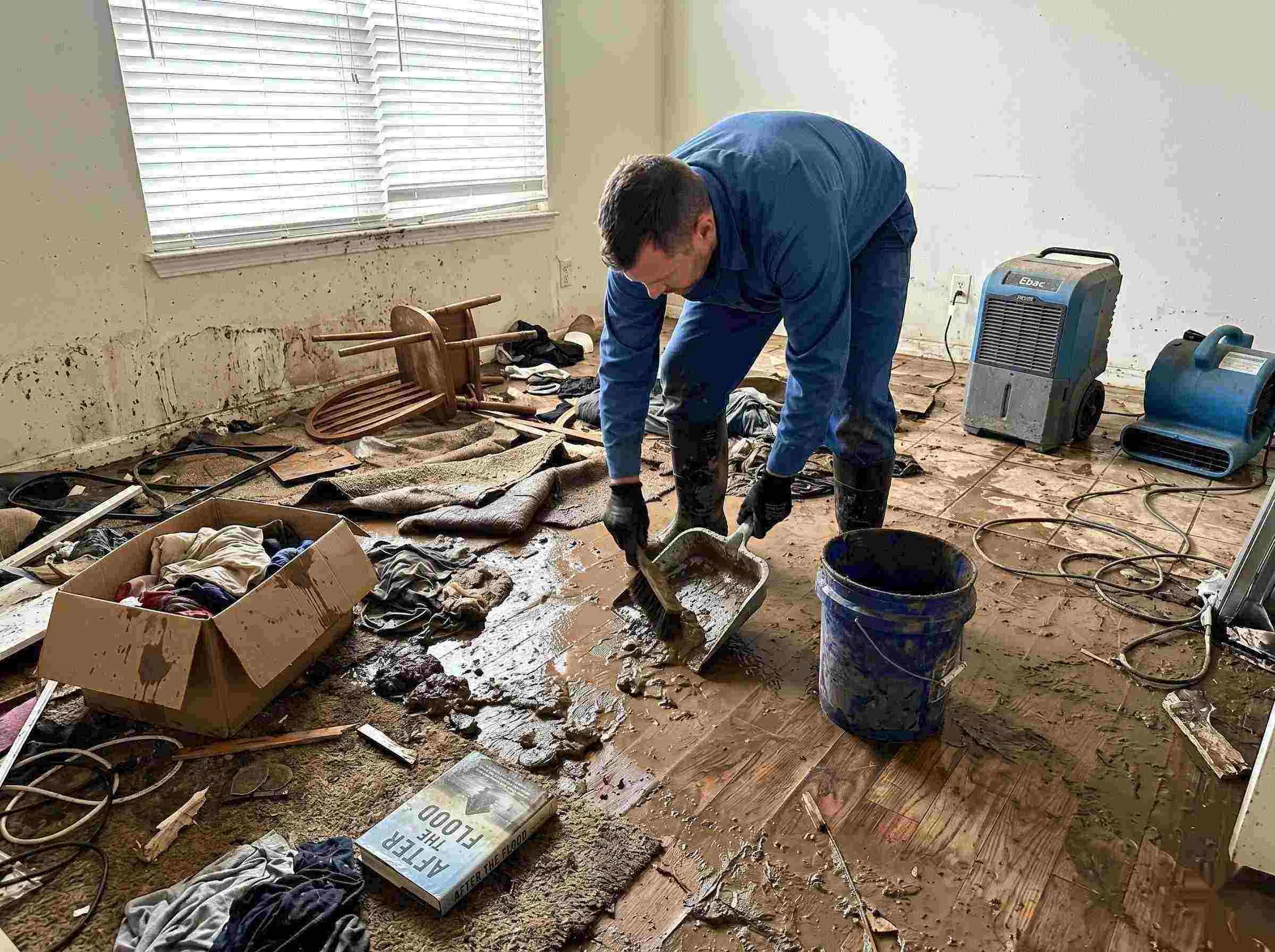 Realistic photo of a technician performing mud and debris removal after a home flood in Wichita, showing soaked furniture, wet flooring, and scattered debris during post-flood cleanup.